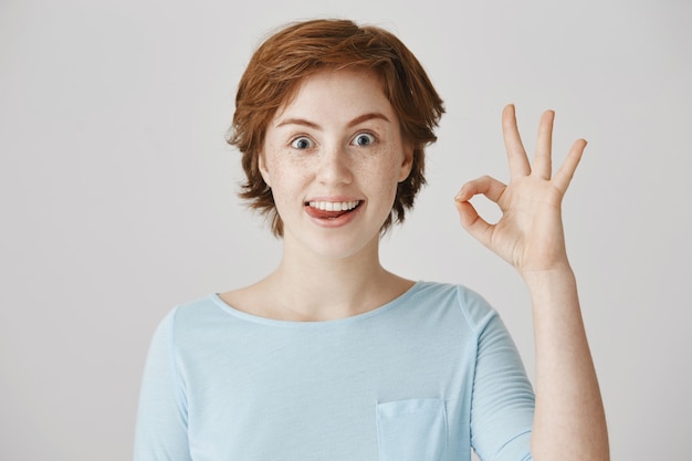 Joyeuse fille rousse excitée posant contre le mur blanc