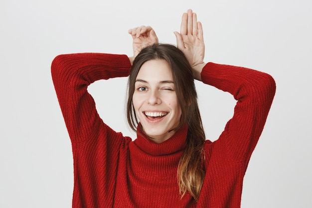 Joyeuse fille souriante clin d'oeil et montre le geste des oreilles de lapin