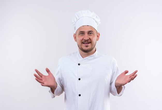 Joyeuse jeune belle cuisinière en uniforme de chef montrant les mains vides isolées sur le mur blanc