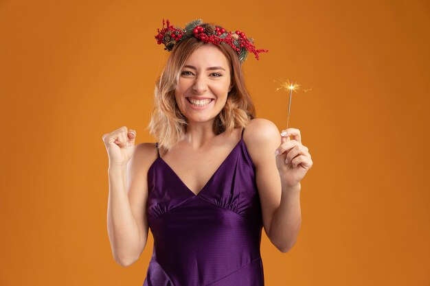 Joyeuse jeune belle fille vêtue d'une robe violette avec une couronne tenant des cierges magiques montrant un geste oui isolé sur fond marron