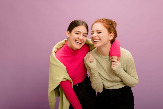 Joyeuse jeune brune caucasienne et rousse en vêtements décontractés passent du temps ensemble sur fond violet Concept de mode de vie actif de loisirs pour les jeunes