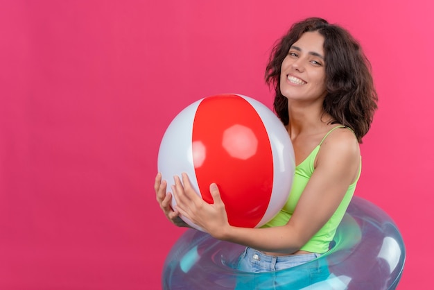 Une joyeuse jeune femme aux cheveux courts en vert crop top souriant et tenant ballon gonflable