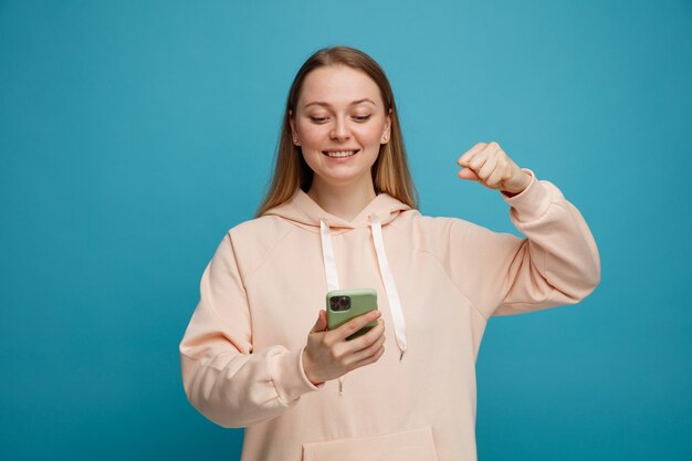 Joyeuse jeune femme blonde tenant et regardant le téléphone mobile faisant oui geste