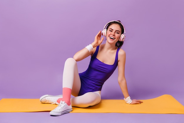 Joyeuse jeune femme en body violet et collants blonds, écouter de la musique avec le sourire