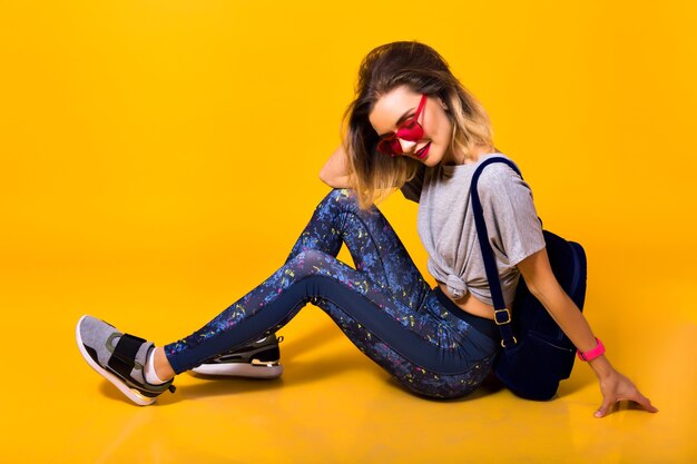 Joyeuse jeune femme en leggings de sport et baskets à la mode s'amuser en studio