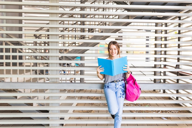 Photo gratuite joyeuse jeune femme lisant un livre près du mur