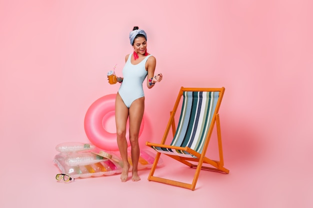 Joyeuse jeune femme en maillot de bain blanc dansant près de chaise longue