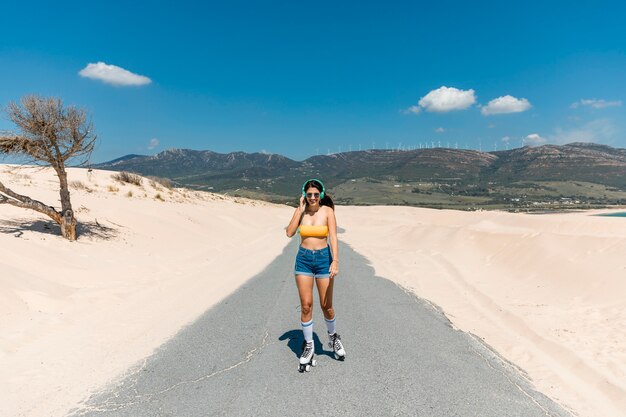 Joyeuse jeune femme patinant sur une route sablonneuse