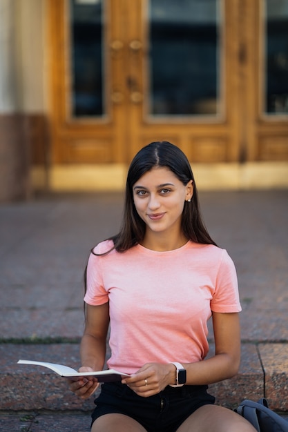 Joyeuse jeune femme prenant des notes assise sur des marches dans la rue