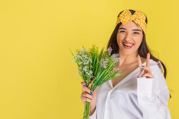 Photo gratuite joyeuse jeune femme tenant un bouquet de fleurs et faisant des gestes de paix