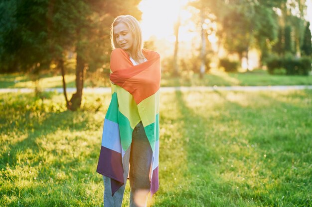 Joyeuse jeune femme tenant un drapeau arc-en-ciel sur les épaules