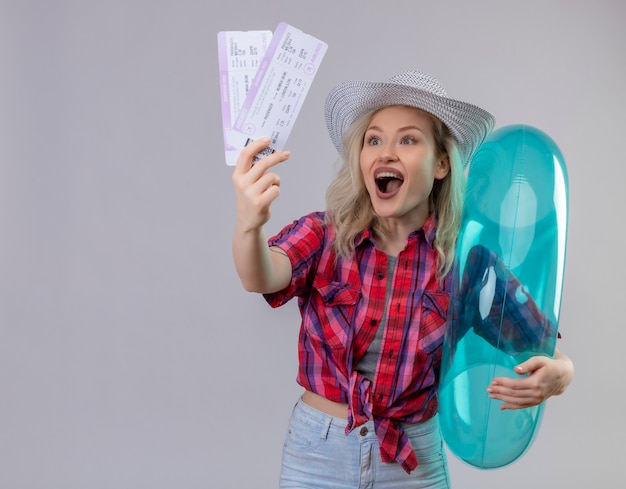 Photo gratuite joyeuse jeune femme voyageur portant une chemise rouge au chapeau tenant un anneau gonflable et des billets sur un mur blanc isolé