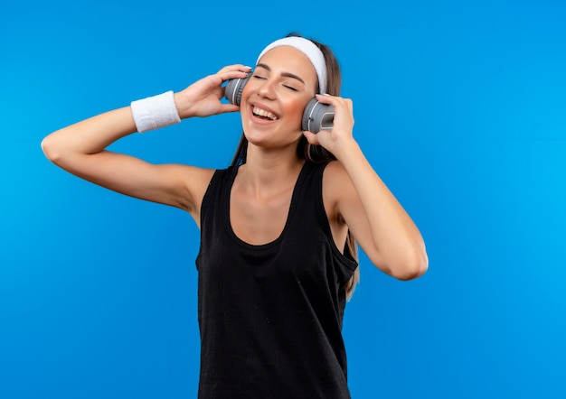 Joyeuse jeune fille assez sportive portant bandeau et bracelet et écouteurs écoutant de la musique avec les yeux fermés sur l'espace bleu