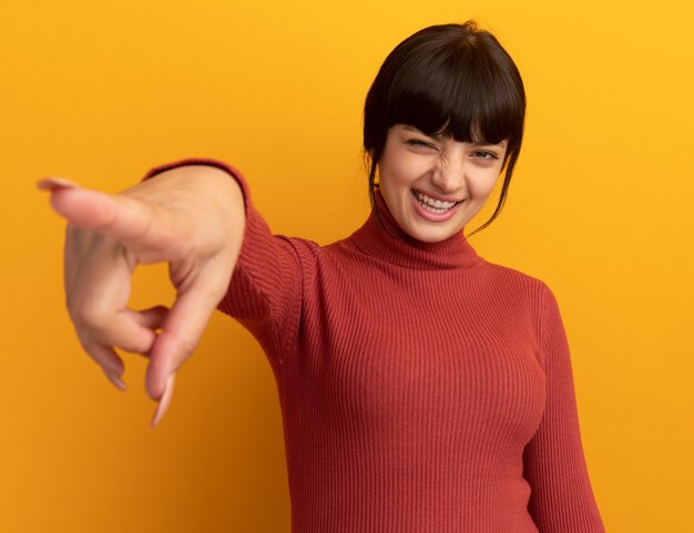 Joyeuse jeune fille brune caucasienne clignote des yeux et pointe sur le côté orange