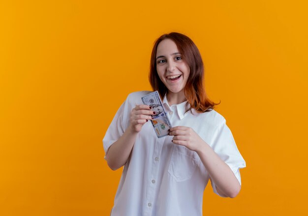 Joyeuse jeune fille rousse tenant de l'argent isolé sur fond jaune avec espace de copie