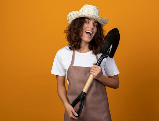 Joyeuse jeune jardinière en uniforme portant chapeau de jardinage holding spade