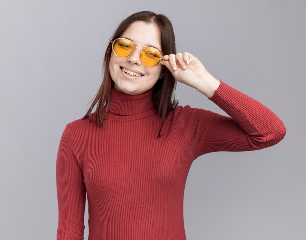 Joyeuse jeune jolie fille portant et saisissant des lunettes de soleil