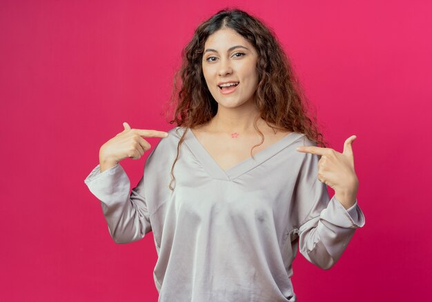 Joyeuse jeune jolie fille se pointe isolée sur fond rose