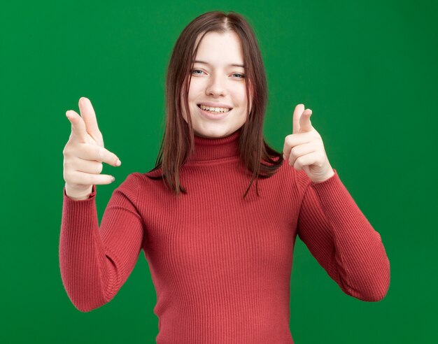 Joyeuse jeune jolie fille vous faisant un geste isolé sur un mur vert