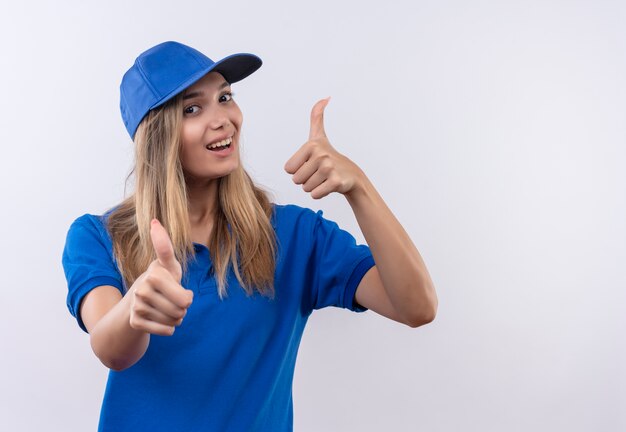 Joyeuse jeune livreuse portant l'uniforme bleu et capuchon ses pouces vers le haut isolé sur un mur blanc avec espace copie