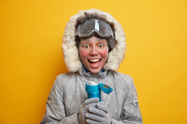 Joyeuse jeune touriste active active le snowboard en hiver porte une veste chaude et des gants recouverts de boissons glacées le thé chaud a un repos enneigé génial station saisonnière activités de plein air de loisirs