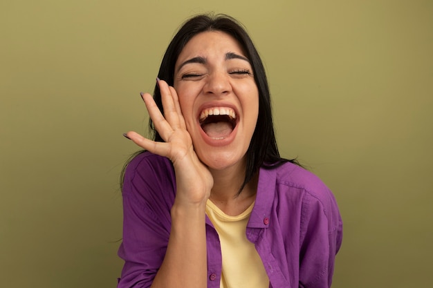 Joyeuse jolie fille caucasienne brune tient la main près de la bouche sur vert olive