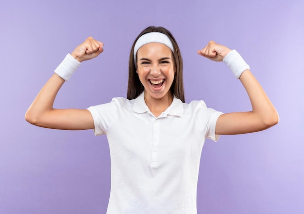 Photo gratuite joyeuse jolie fille sportive portant un bandeau et un bracelet faisant des gestes forts isolés sur un mur violet