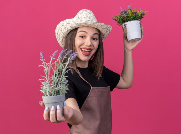 Joyeuse jolie jardinière caucasienne portant un chapeau de jardinage tenant des pots de fleurs