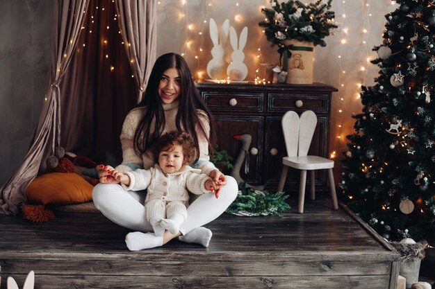 Joyeuse maman joue avec son jeune enfant dans l'atmosphère de Noël dans la chambre