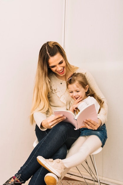 Photo gratuite joyeuse mère et fille lisant un livre sur chaise