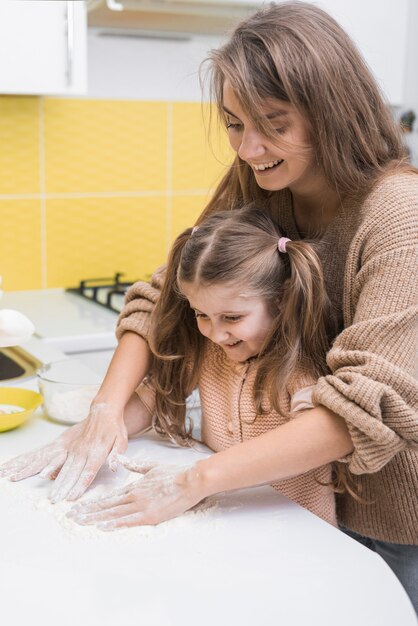 Joyeuse mère et fille mettant la farine sur la table