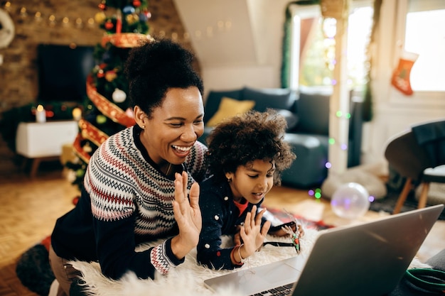 Joyeuse mère et fille noires saluant quelqu'un lors d'un appel vidéo à Noël