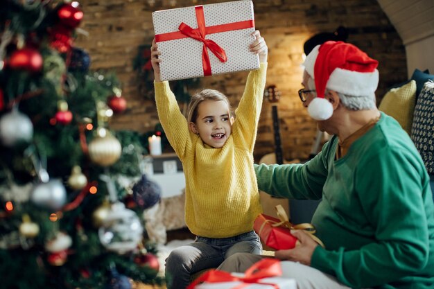Joyeuse petite fille s'amusant à Noël tout en recevant un cadeau de grand-père