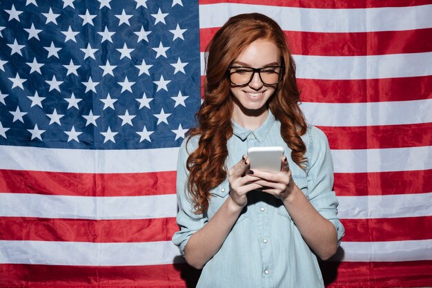 Joyeuse rousse jeune femme debout sur le drapeau des États-Unis bavarder