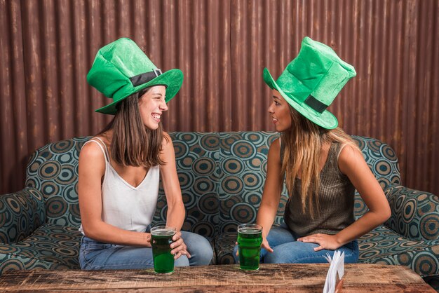 Joyeuses jeunes femmes avec des verres de boisson sur le canapé dans la chambre