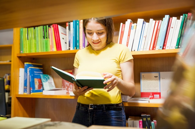Joyeux adolescent lisant derrière la bibliothèque