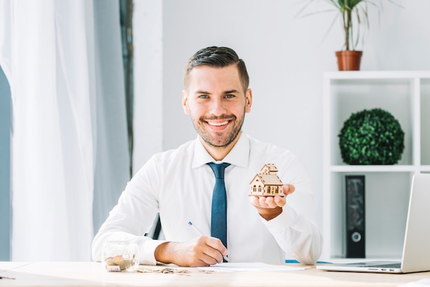 Photo gratuite joyeux agent immobilier montrant la maison de jouet