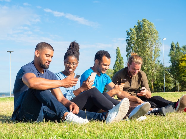 Joyeux amis multiethniques à l'aide de smartphones dans le parc