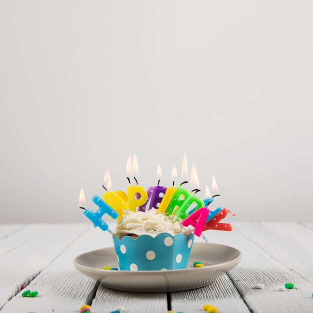 Joyeux anniversaire lettre bougies sur le petit gâteau sur une plaque en céramique sur fond blanc