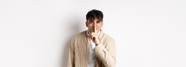 Joyeux bel homme à lunettes partage un secret faisant la surprise se pencher à la caméra avec un geste de silence et