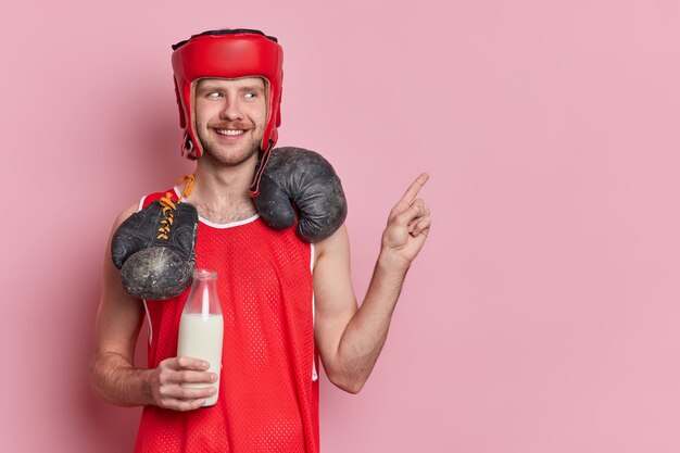 Joyeux boxeur vêtu de vêtements de sport boit du lait comme source de protéines porte des gants de boxe autour du cou indique à l'espace copie vierge