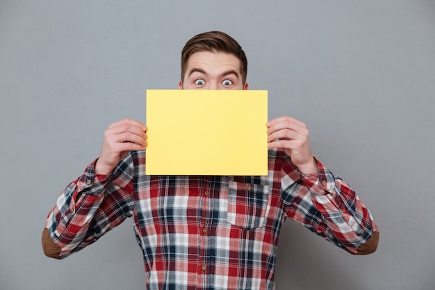 Joyeux choqué jeune homme barbu tenant du papier vierge