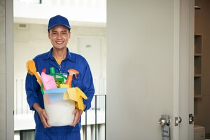 Photo gratuite joyeux concierge asiatique mâle marchant dans la chambre d'hôtel, transportant des fournitures dans le seau