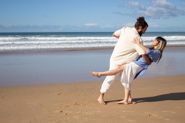 Joyeux couple caucasien dansant pieds nus à la plage