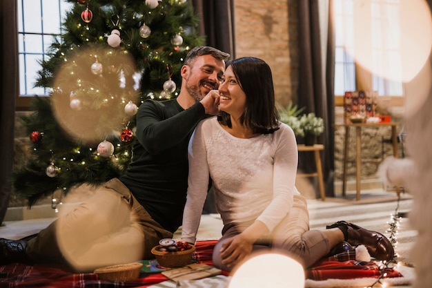 Joyeux couple de personnes âgées avec des lumières et arbre de Noël derrière