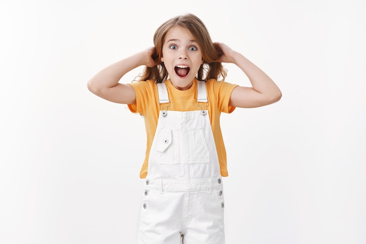 Photo gratuit joyeux enfant excité s'amusant, debout enjoué et surpris, fille touchant les cheveux en soulevant la coupe de cheveux dans l'air, criant amusé et joyeux, exprime une humeur joyeuse et enthousiaste, se tient debout sur un mur blanc