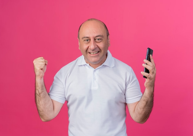 joyeux homme d'affaires mature tenant le téléphone mobile serrant le poing faisant oui geste