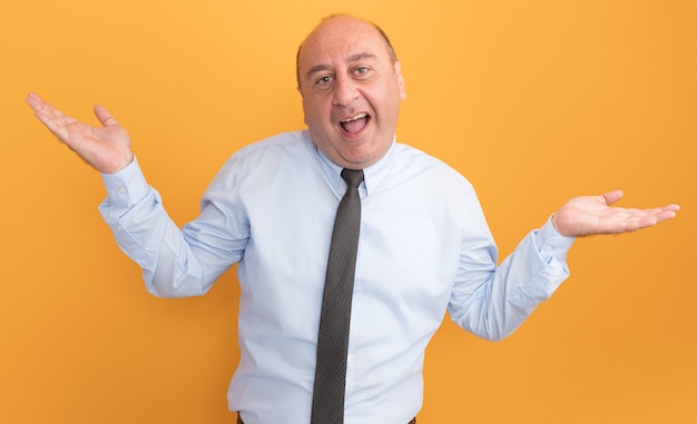 Joyeux homme d'âge moyen portant un t-shirt blanc avec une cravate répandant les mains isolé sur un mur orange