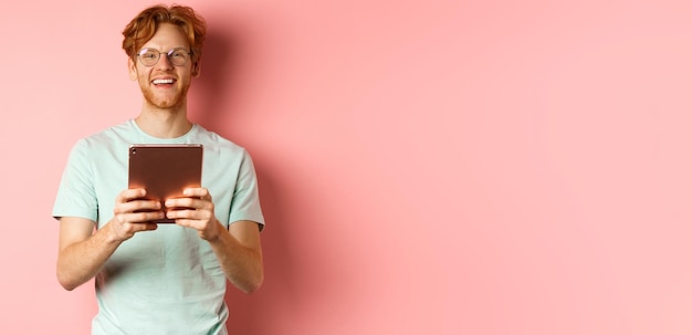 Photo gratuite joyeux homme caucasien en t-shirt et lunettes à l'aide d'une tablette numérique à la recherche de plaisir à l'appareil photo et smilin