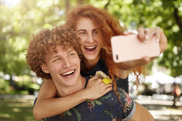 Joyeux homme et femme se reposant à l'extérieur en prenant des selfies